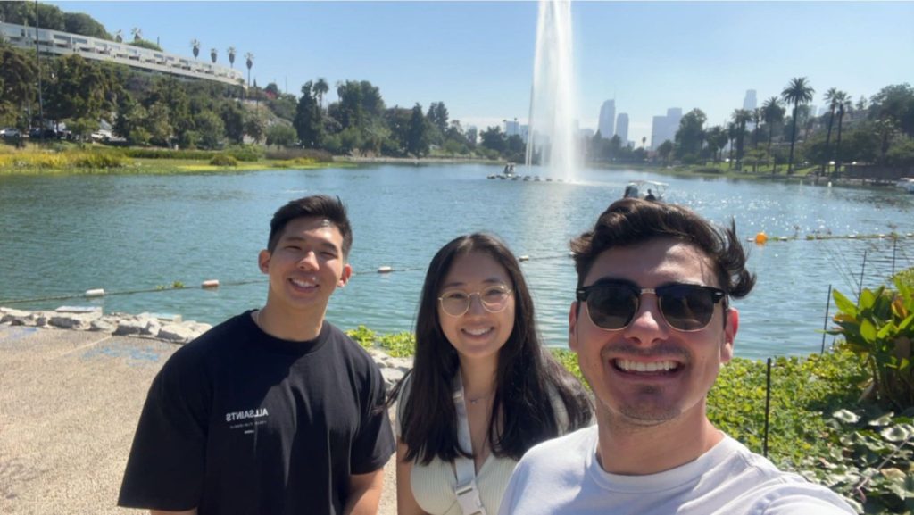 three law students standing in front of a small lake wit a fountain in the background
