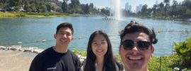 three law students standing in front of a small lake wit a fountain in the background